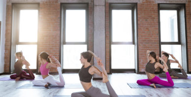 Young women forming circle on mats in fitness center exercising yoga poses